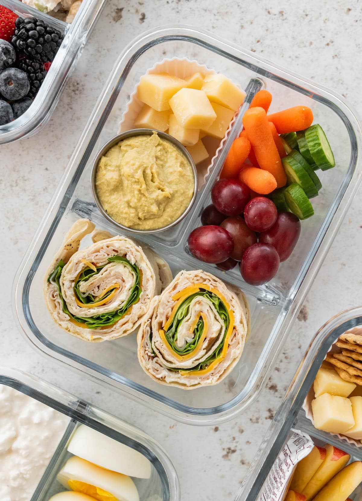 Turkey pinwheel protein box with parmesan cubes, hummus, baby carrots, cucumber and red grapes.